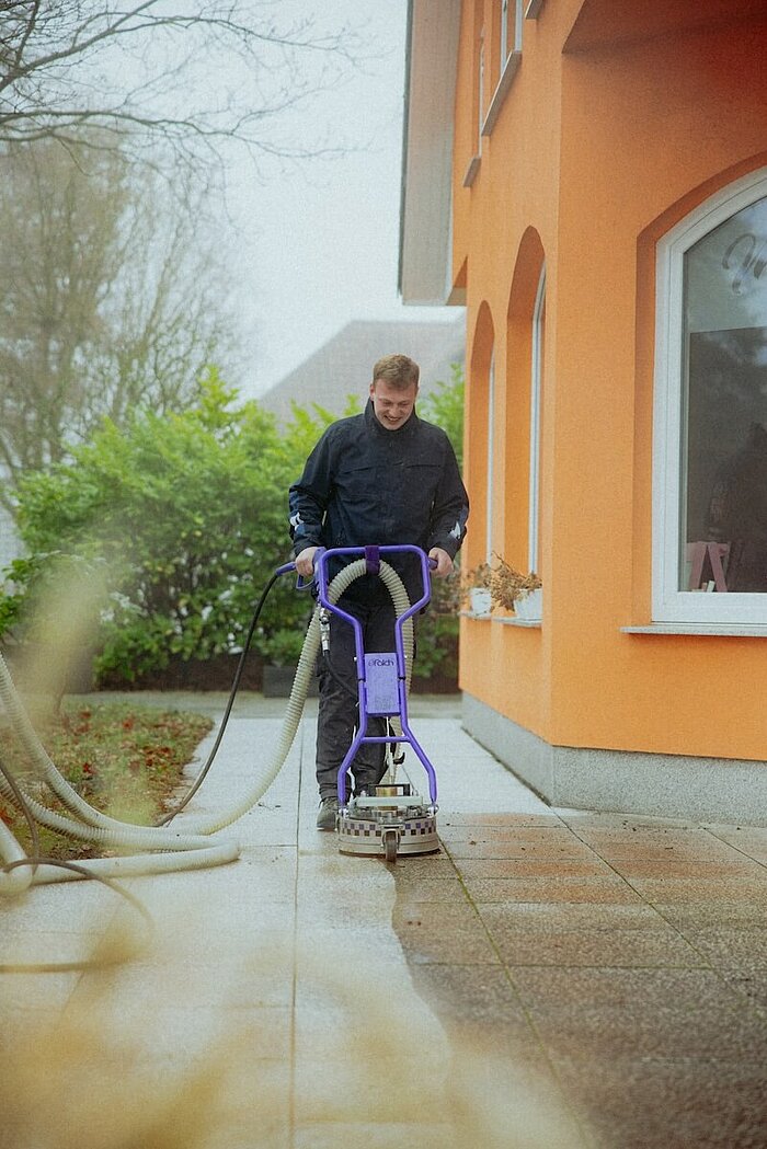 Das Bild zeigt einen Facharbeiter bei der professionellen Steinflächenreinigung mit deutlich sichtbaren Ergebnissen.