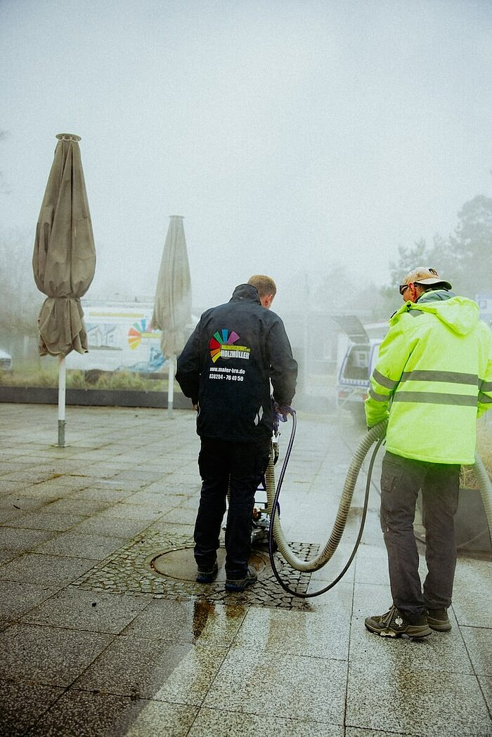Das Bild zeigt zwei Facharbeiter bei der professionellen Oberflächenreinigung mit Heißwasser-Hochdruckreiniger.