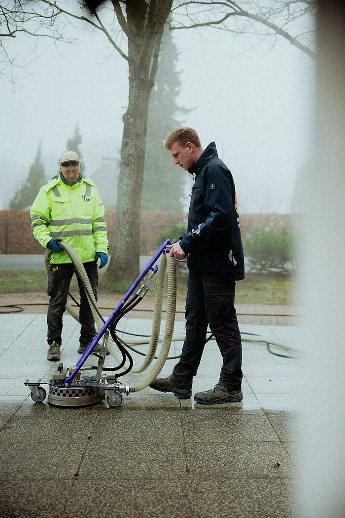 Zwei Mitarbeiter der Malergesellschaft Holzmüller führen eine professionelle Steinreinigung mit einem modernen Heißwasser-Hochdruckreiniger durch.